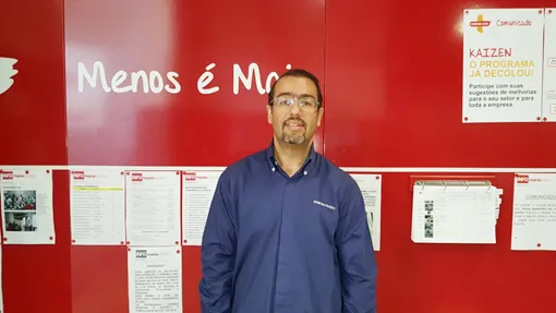 Homem diante de painel vermelho de comunicação com o cartaz Kaizen o programa já decolou