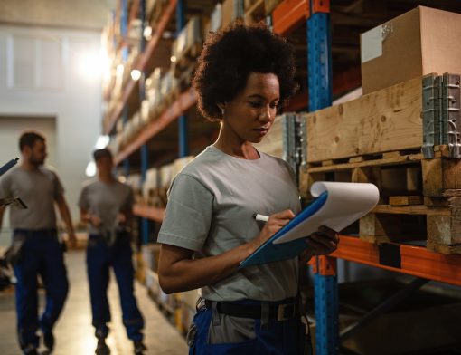 Black female warehouse worker writing delivery schedule list.