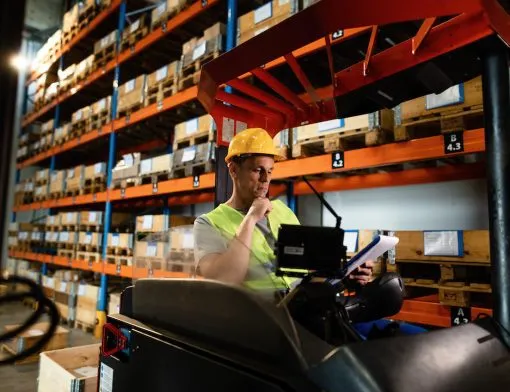 Forklift operator going through shipment schedule list in a warehouse.